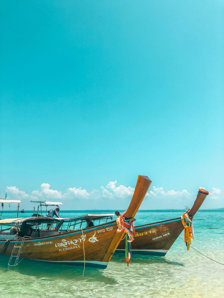 A cinematic photo of a private long-tail boat resting on the turquoise waters of a secluded, beautiful cove in Phuket, Thailand, representing a serene and exclusive family adventure.